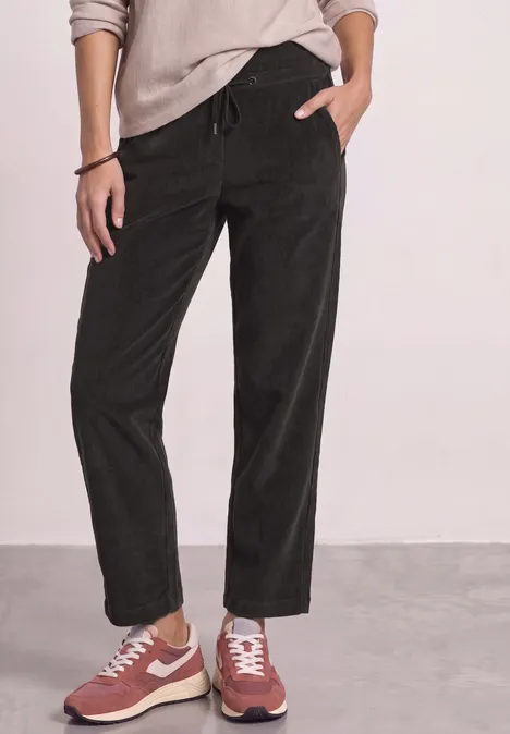 Person trägt schwarze Cordhose und rote Sneaker