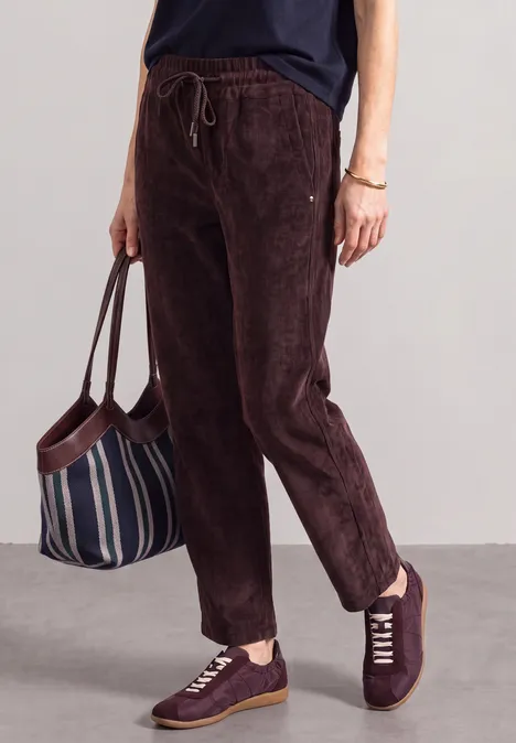 Person trägt dunkelbraune Cordhose, bordeauxrote Sneaker und hält eine gestreifte Stofftasche.