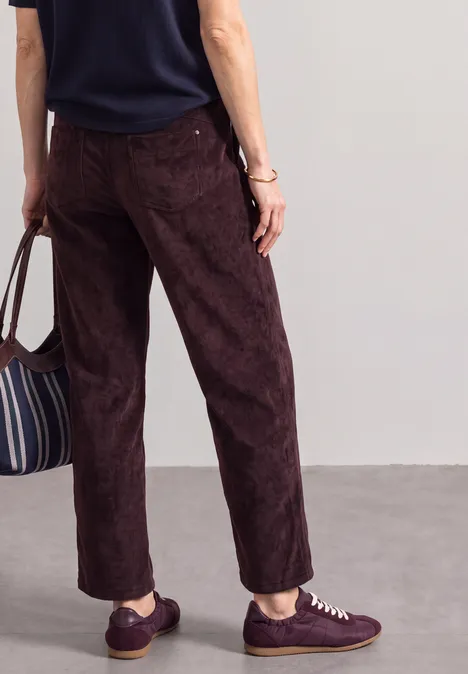 Rückansicht einer Person mit dunkelbraunen Hosen, violetten Sneakern und gestreifter Tasche.