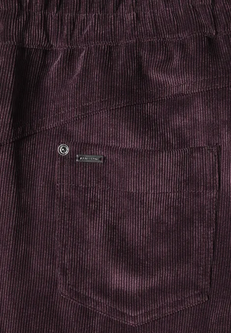 Nahaufnahme einer violetten Cordhose mit Tasche und Logo-Label.
