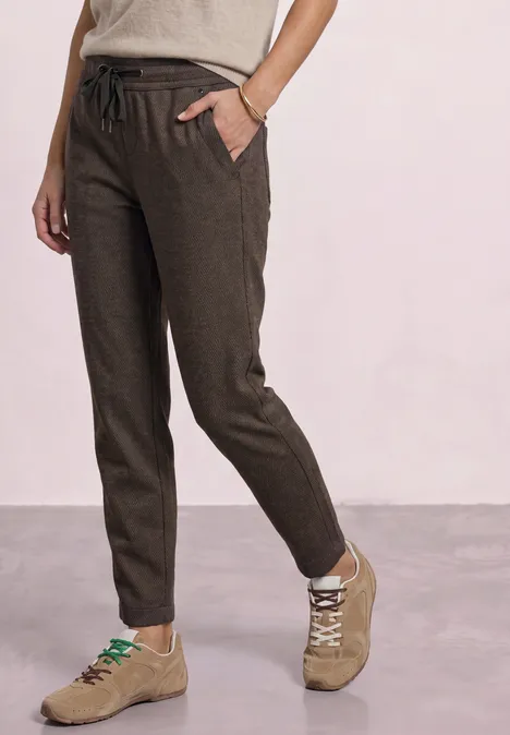 Dunkelbraune Leinenhose mit Tunnelzug, schmale Passform und Seitentaschen, kombiniert mit beigen Sneakers.