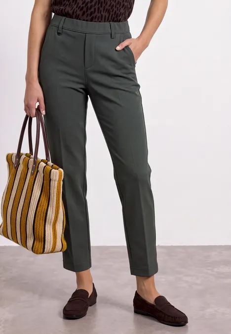 Person trägt olivgrüne, schmale Hose und hält eine große, gelb-weiß gestreifte Tasche.