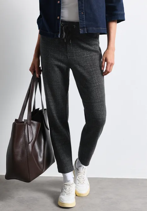 Person trägt graue, locker geschnittene Hose, weiße Sportschuhe und hält eine große braune Tasche.