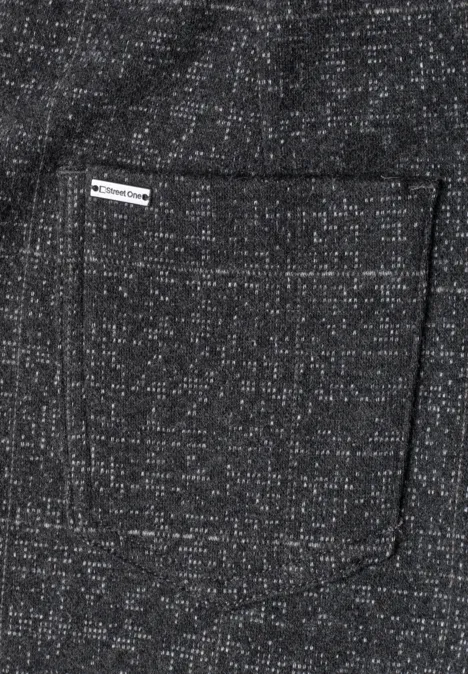 Auf grauem, meliertem Stoff mit weißen Sprenkeln ist eine eckige Tasche mit kleinem Webetikett angebracht.