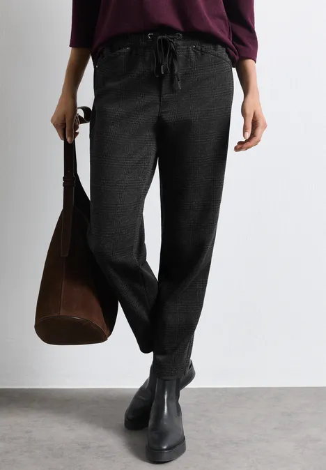 Frau trägt schwarze lockere Hose mit Tunnelzug, schwarze Stiefeletten und hält eine braune Tasche.