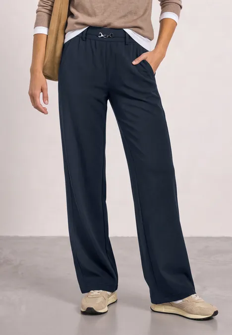Vrouw draagt wijde zwarte broek met trekkoord en beige sneakers.
