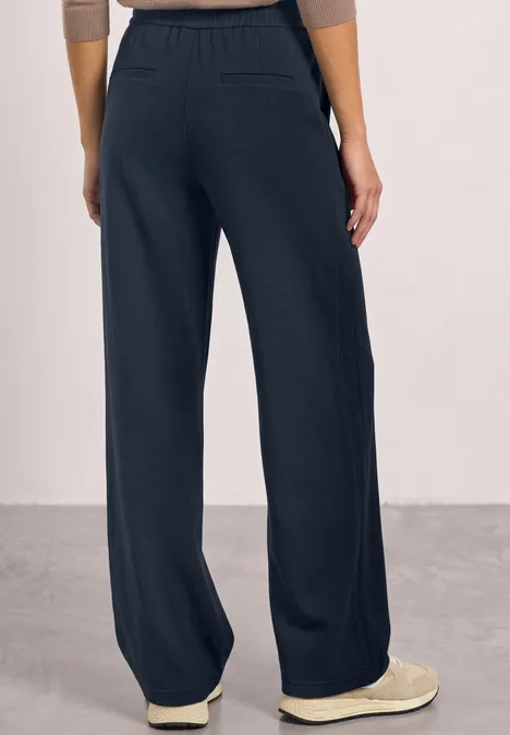 Vrouw met wijde marineblauwe broek met elastische taille en lichte instappers.