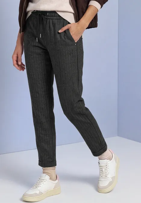 Slim Leg-broek met patroon in een Loose Fit-pasvorm Black Vrouw draagt donkere joggingbroek met fijne strepen, koordceintuurtje en witte sneakers tegen lichte achtergrond.