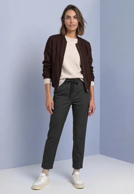 Slim Leg-broek met patroon in een Loose Fit-pasvorm Black Vrouw in bruine vest, crèmekleurige trui, grijze broek en witte sneakers voor een effen muur.