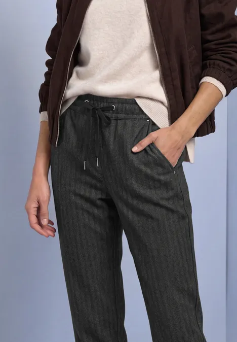 Slim Leg-broek met patroon in een Loose Fit-pasvorm Black Vrouw in donkere pantalon met fijne strepen en trekkoord, gecombineerd met een lichte trui en jas.