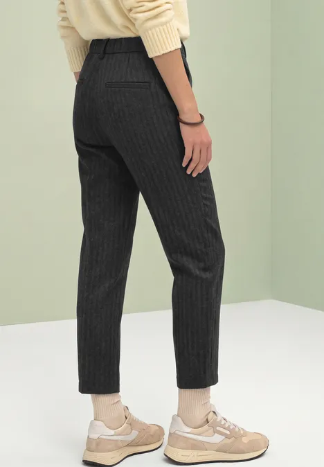 Pantalon à rayures fines noires et blanches porté avec des baskets beiges sur fond clair.