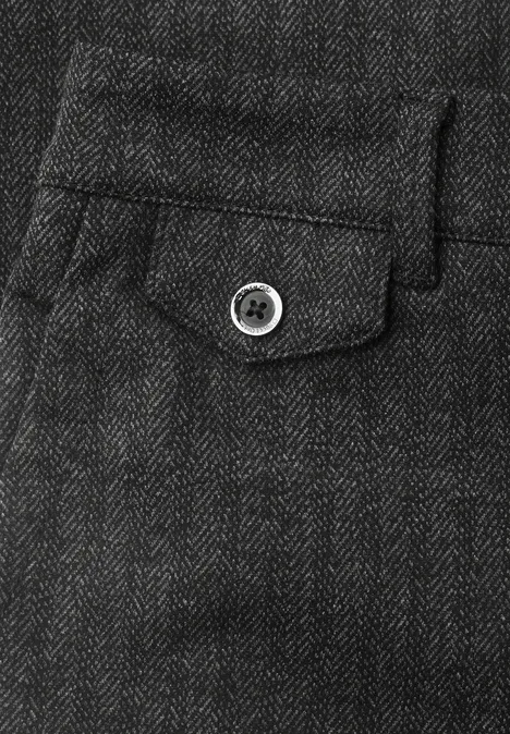 Gros plan d’un pantalon gris foncé en chevrons avec petite poche à rabat et bouton.