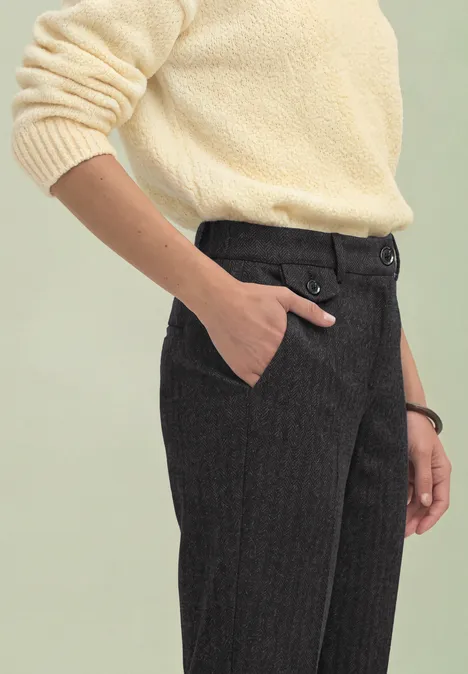 Personne portant un pull crème et un pantalon sombre à fines rayures, main dans la poche.