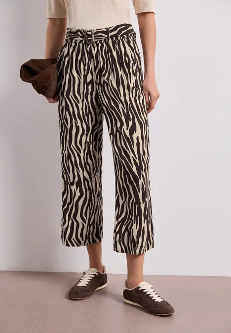 Croppte Hose mit Zebra-Print, weißes Oberteil, braune Clutch und braune Sneaker.