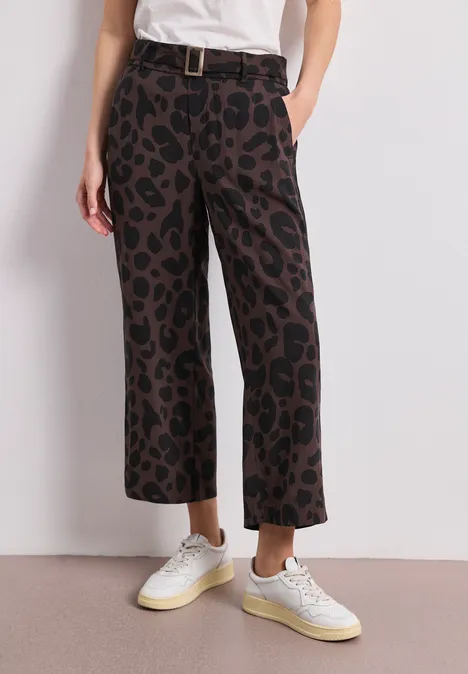 Kurze, weite Damenhose mit braun-schwarzem Leopardenprint, hohem Bund, Gürtel und weißen Sneakern.
