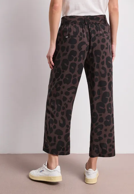 Rückenansicht: Person trägt weiße Sneaker, Culotte-Hose mit braun-schwarzem Leopardenmuster und weißes T-Shirt.