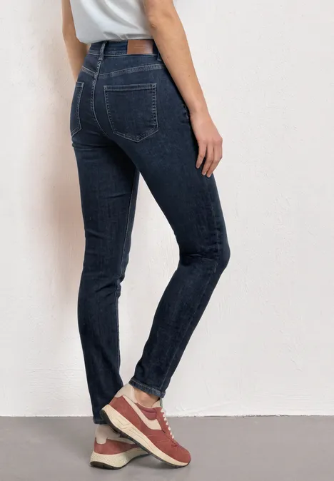 Eine Person in dunklen Skinny-Jeans und roten Sneakern, von hinten vor einer weißen Wand.