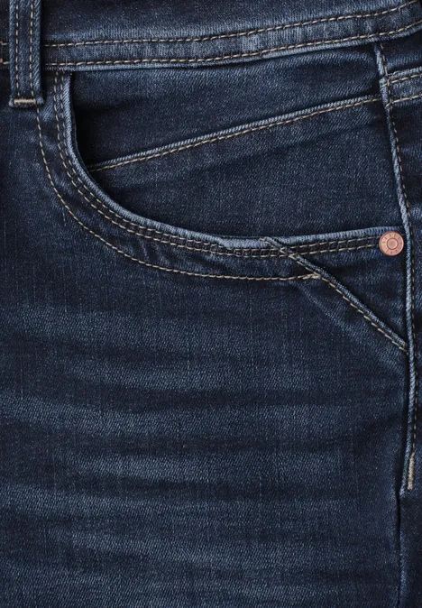 Nahaufnahme einer dunkelblauen Jeans mit sichtbarer Fronttasche, Münztasche, Naht und Metallniete.
