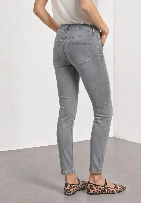 Person von hinten in grauen Jeans und Leo-Ballerinas vor weißem Hintergrund.