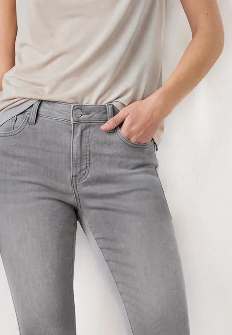 Person mit grauen Jeans und leichtem beigen T-Shirt, Hand in Tasche.