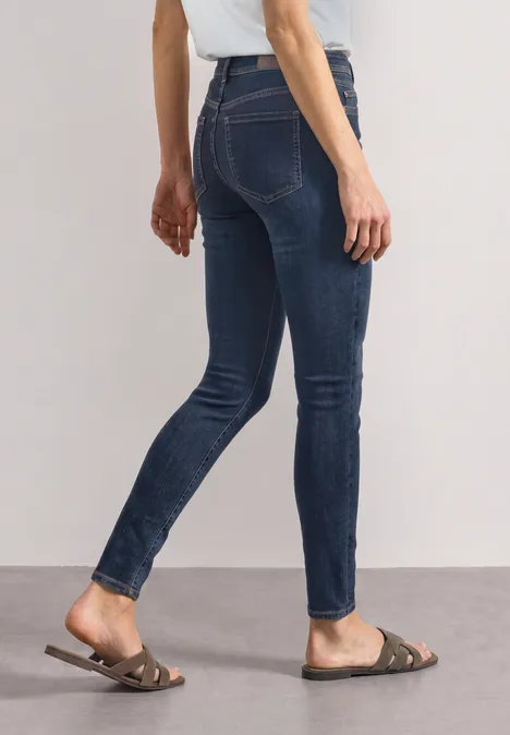Dame trägt dunkelblaue Skinny-Jeans und flache braune Sandalen.