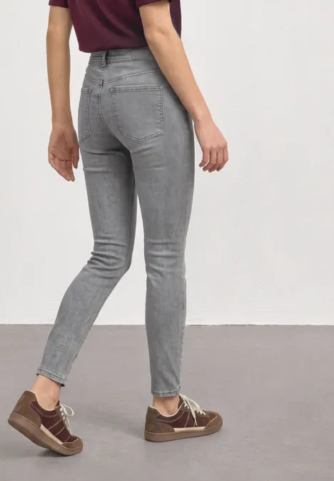 Frau in grauer Skinny-Jeans und braunen Sneakern, von hinten auf neutralem Hintergrund.