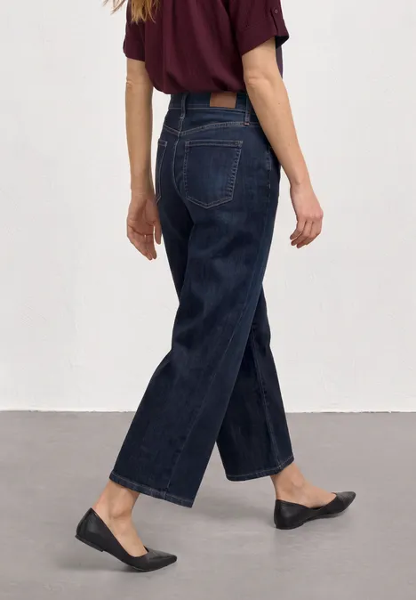 Jeans Culotte mit Gürteldetail Deep Blue Washed Person von hinten in weitem, dunkelblauen Jeans, schwarzen Ballerinas und bordeauxrotem Shirt, Fokus auf Unterkörper.