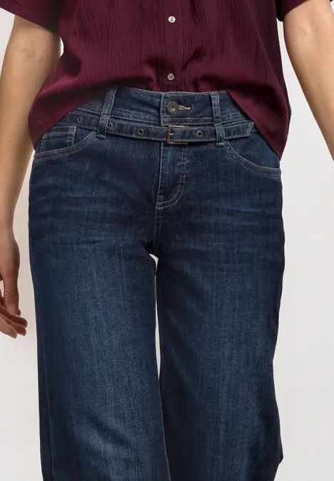 Jeans Culotte mit Gürteldetail Deep Blue Washed Frau trägt dunkelblaue High-Waist-Jeans mit doppeltem Taillengürtel und kastigem kurzärmeligem weinroten Oberteil.