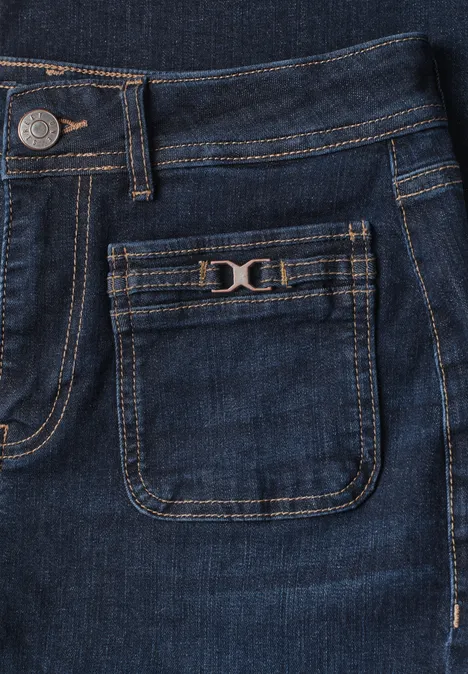Detailaufnahme einer dunkelblauen Jeans mit kleiner Fronttasche, Metallknopf und Ziernaht.