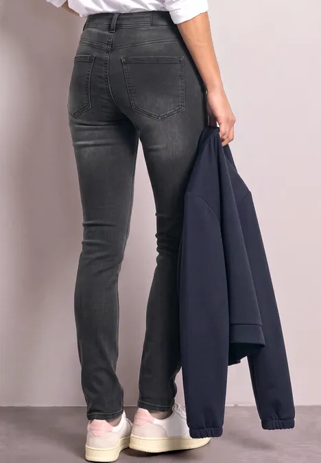 Person trägt enge, schwarze Jeans und weiße Sneaker, hält eine dunkelblaue Jacke in der Hand.
