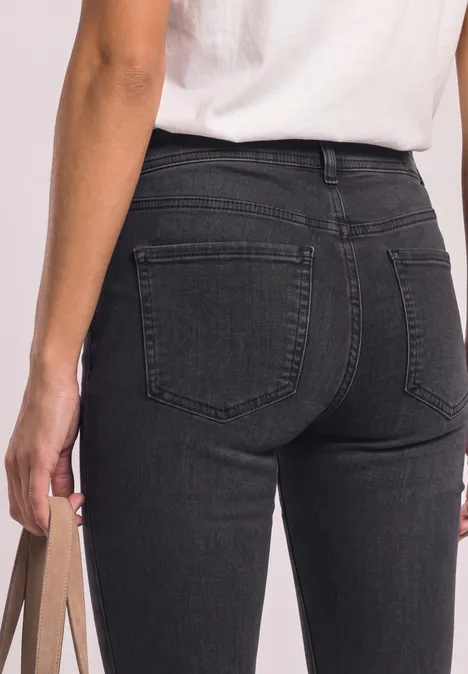 Zbliżenie osoby od tyłu w czarnych jeansach i białym T-shircie, trzyma torbę w dłoni.