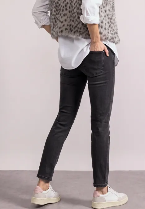 Mid Waist Straight Leg Jeans im Slim Fit Black Washed Person von hinten in schwarzen Slim-Jeans, weißem Hemd, grauer Leopardenweste und weißen Sneakern.