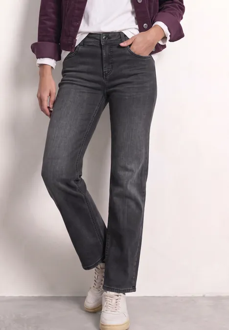 Graue High-Waist-Jeans mit geradem Bein, kombiniert mit weißem T-Shirt, lila Blouson und weißen Sneakern.