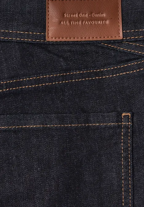Mid Waist Slim Leg Jeans w Casual Fit Deep Rinse Washed Zbliżenie ciemnoniebieskich dżinsów z pomarańczowymi szwami i skórzaną metką nad tylną kieszenią.