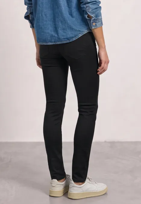 Mid Waist Slim Leg jeans im Slim Fit Black Clean Washed Frau steht mit schwarzer enger Hose und weißen Sneakern, Rückenansicht.