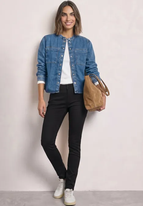 Mid Waist Slim Leg jeans im Slim Fit Black Clean Washed Frau trägt Jeansjacke, weißes Shirt, schwarze Hose, weiße Sneaker und hält eine braune Tasche.