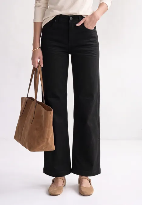 Van de taille naar beneden: wijde zwarte broek, wit top, beige loafers en grote bruine suède tas.