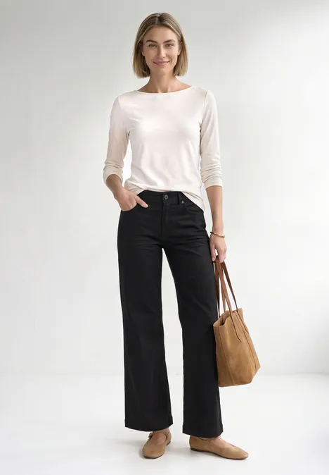 Vrouw lachtend in witte top, zwarte wijde broek, bruine loafers en beige tas.