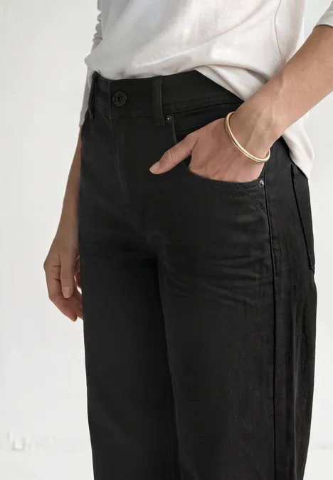 Eenvoudige look met zwarte jeans en wit shirt, hand in voorzak gestoken.