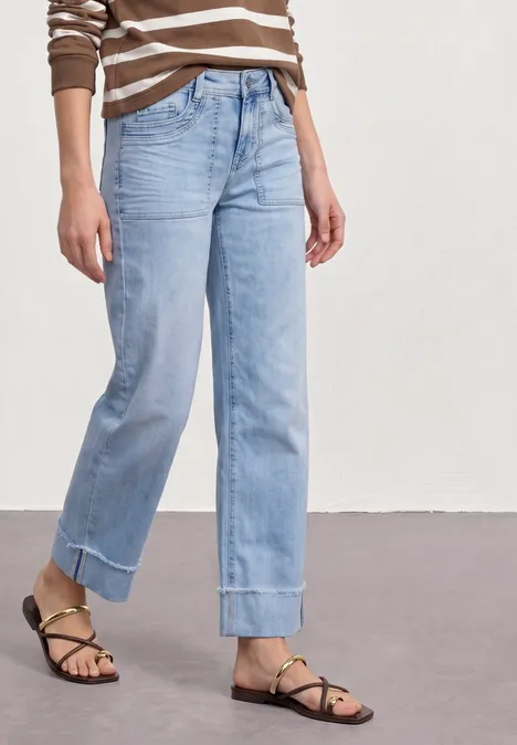Frau trägt gestreiftes Oberteil, helle weite Jeans mit Umschlag und schwarze Riemchensandalen.