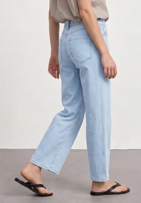 Mid Waist Wide Leg Jeans im Loose Fit Ultra Bleached Wash Seitenansicht einer Person mit hellblauen, geraden Jeans und schwarzen Flip-Flops.