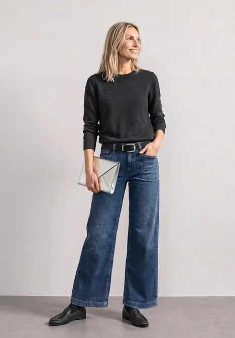 Eine Frau in schwarzem Pullover, weiten Jeans und schwarzen Stiefeln mit silberner Clutch.