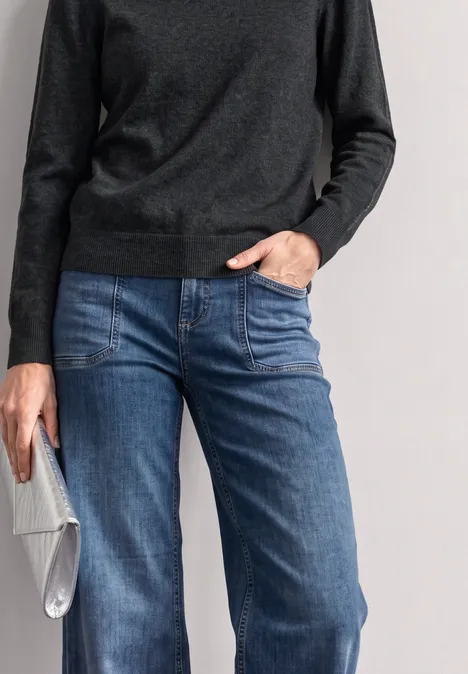 Person trägt dunklen Pullover, blaue Jeans und hält eine silberne Clutch.