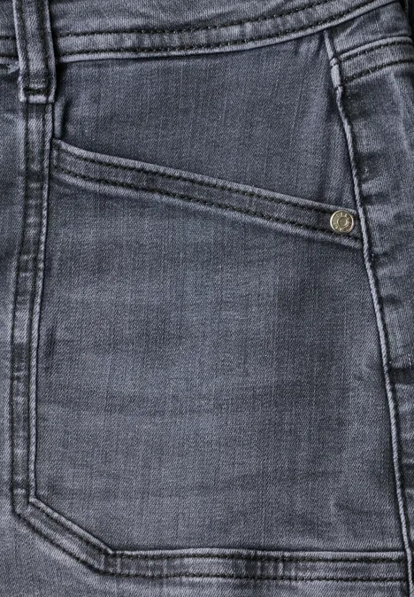 Close-up van een donkergrijze spijkerbroekzak met schuine muntzak, metalen knoop en zichtbare stiksels.