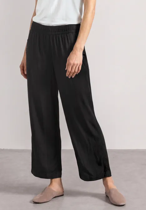 High Waist Wide Leg Hose im Loose Fit Black Schwarze, weite Hose mit Gummibund und grauen Slippern vor neutralem Hintergrund.