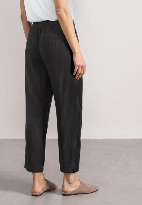 High Waist Wide Leg Hose im Loose Fit Black Ein Modell von hinten in schwarzen, lässigen, hoch geschnittenen Hosen mit elastischem Bund und beigen Slippern.