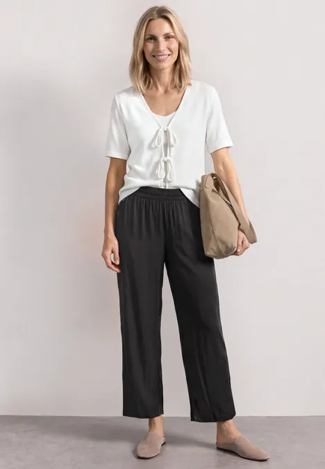 High Waist Wide Leg Hose im Loose Fit Black Frau trägt weißes T-Shirt, schwarze weite Hose, beige Schuhe, hält Papiertüte.