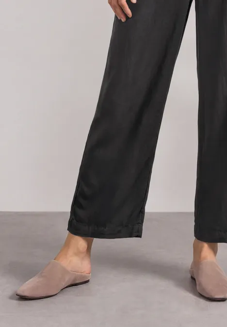 High Waist Wide Leg Hose im Loose Fit Black Person trägt schwarze weite Hose und graue Mules auf grauem Boden.