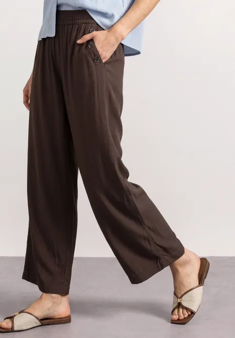Braune, weite Hose mit Gummibund und Eingrifftaschen, kombiniert mit beigen Sandalen.
