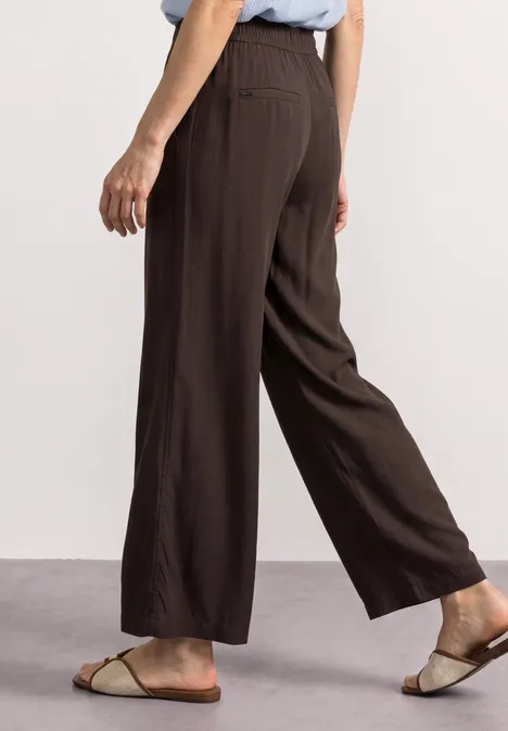 Pantalon large marron 7/8 en lin, porté avec des sandales plates.